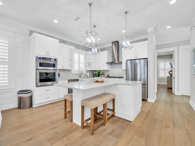 kitchen featuring a center island, wall chimney exhaust hood, stainless steel appliances, and light wood-type flooring