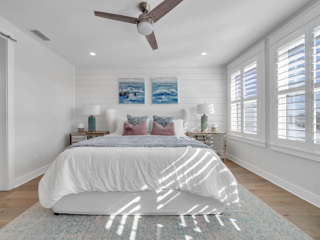 bedroom with light hardwood / wood-style floors, ceiling fan, and wooden walls