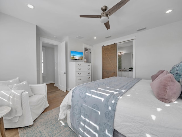 bedroom with connected bathroom, a barn door, ceiling fan, and wood-type flooring