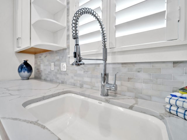 room details featuring white cabinets, light stone counters, and sink