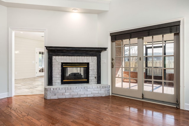 unfurnished living room featuring a brick fireplace, wood finished floors, and a healthy amount of sunlight