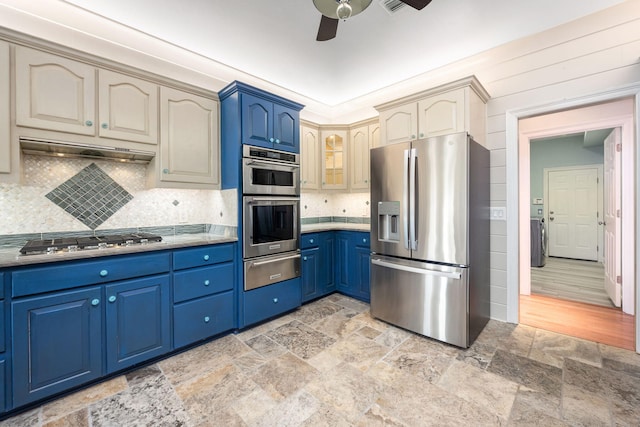 kitchen with blue cabinetry, backsplash, under cabinet range hood, appliances with stainless steel finishes, and a warming drawer