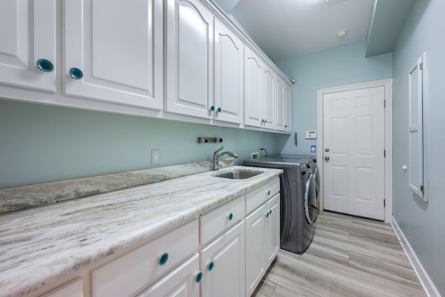 clothes washing area with baseboards, washing machine and dryer, light wood-style flooring, cabinet space, and a sink