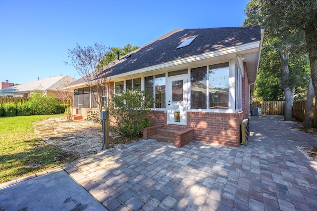 rear view of house with a sunroom, brick siding, a patio, and fence