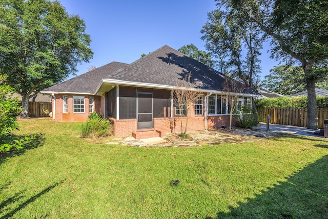 back of property featuring brick siding, a fenced backyard, a lawn, and a sunroom