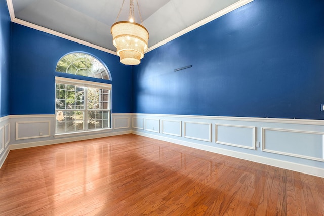 empty room with a notable chandelier, wood finished floors, wainscoting, and a decorative wall