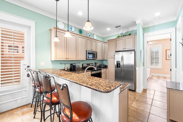 kitchen featuring pendant lighting, dark stone counters, a breakfast bar area, ornamental molding, and stainless steel appliances