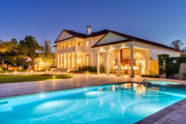 pool at dusk featuring a patio area and an in ground hot tub