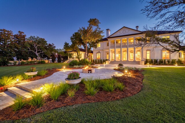 back house at dusk featuring a balcony, a fire pit, and a lawn