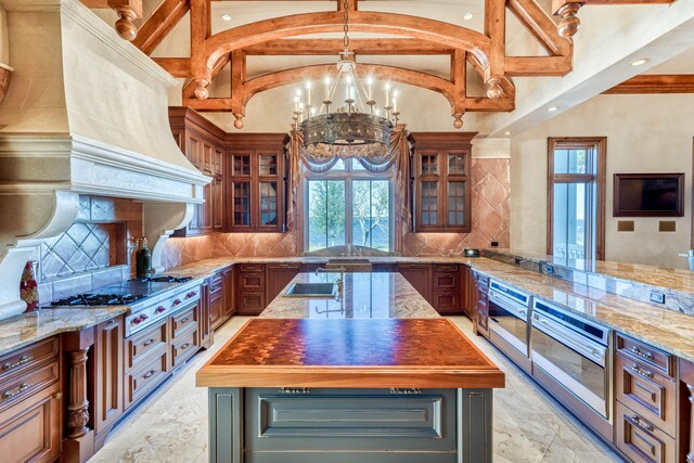 kitchen with hanging light fixtures, stainless steel appliances, a notable chandelier, backsplash, and a kitchen island with sink