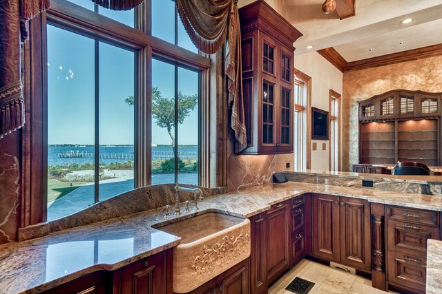 kitchen with a water view, light stone counters, crown molding, and sink