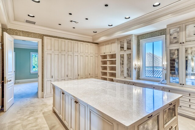 kitchen with light carpet, cream cabinetry, a kitchen island, and light stone countertops