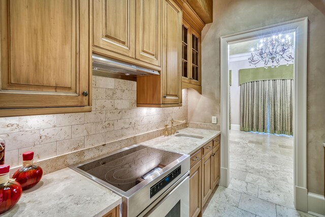 kitchen featuring tasteful backsplash, stainless steel range, ventilation hood, sink, and a chandelier