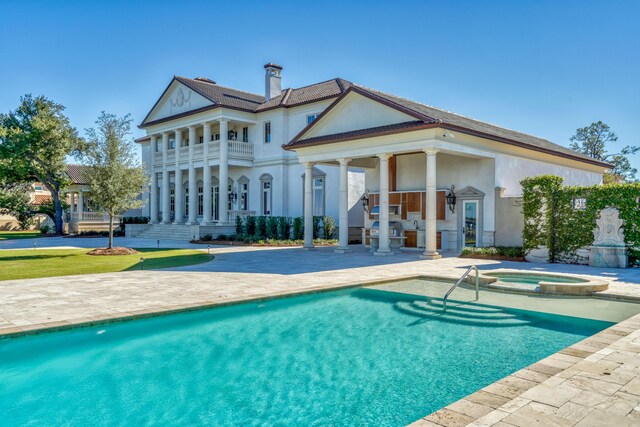 rear view of property featuring a patio, a balcony, and a pool with hot tub