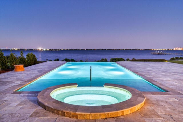 pool at dusk featuring a water view, a patio, and an in ground hot tub