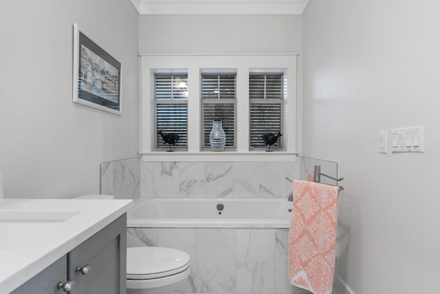 bathroom with tiled tub, vanity, and toilet