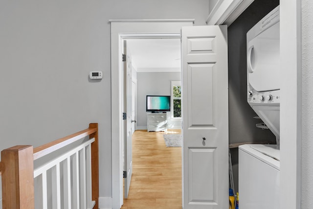 laundry area with light wood-type flooring, stacked washer / dryer, and ornamental molding