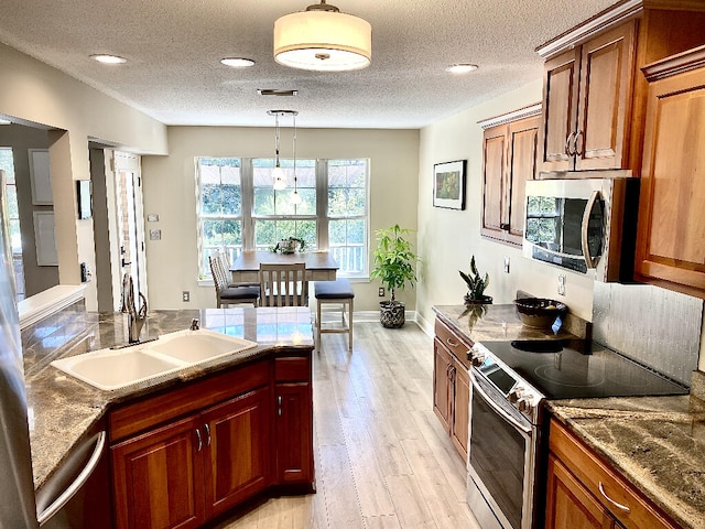 kitchen with a textured ceiling, appliances with stainless steel finishes, sink, hanging light fixtures, and light hardwood / wood-style flooring