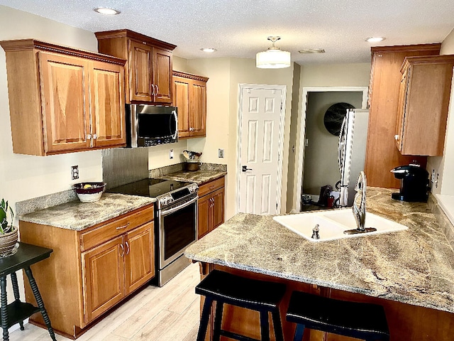 kitchen with stainless steel appliances, a kitchen breakfast bar, light wood-type flooring, a textured ceiling, and sink