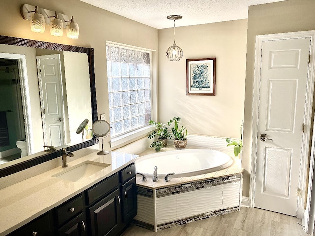 bathroom featuring vanity, wood-type flooring, a relaxing tiled tub, and a textured ceiling