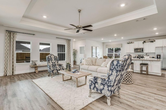 living room featuring light wood-type flooring, a tray ceiling, and ceiling fan