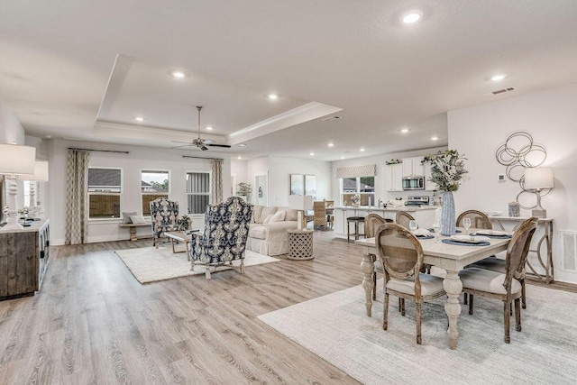 dining area featuring a tray ceiling, ceiling fan, and light hardwood / wood-style flooring