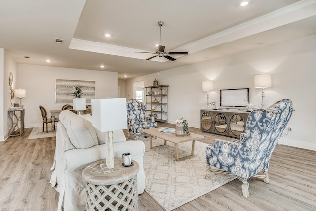 living room featuring a raised ceiling, ceiling fan, and light wood-type flooring