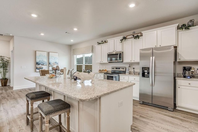 kitchen featuring white cabinets, an island with sink, appliances with stainless steel finishes, and light hardwood / wood-style flooring