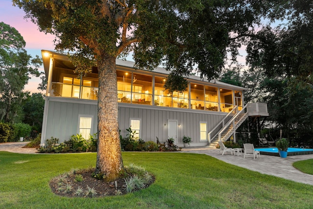 back house at dusk with a lawn, a patio area, and a sunroom