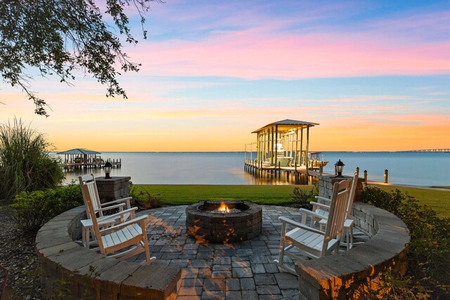 patio terrace at dusk with a water view, a yard, and an outdoor fire pit