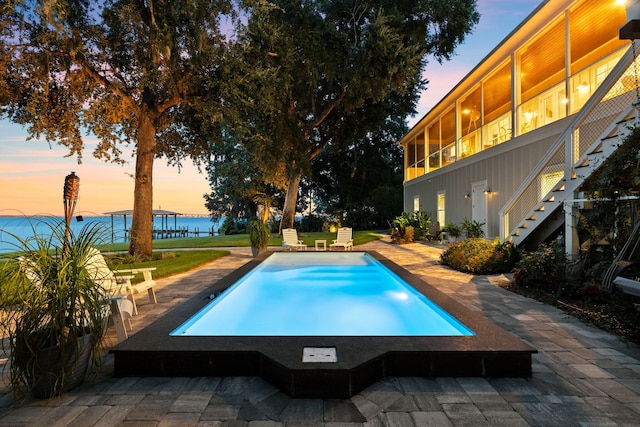 pool at dusk featuring a water view and a patio