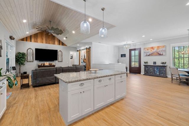 kitchen with white cabinets, hanging light fixtures, a barn door, a kitchen island, and light stone counters