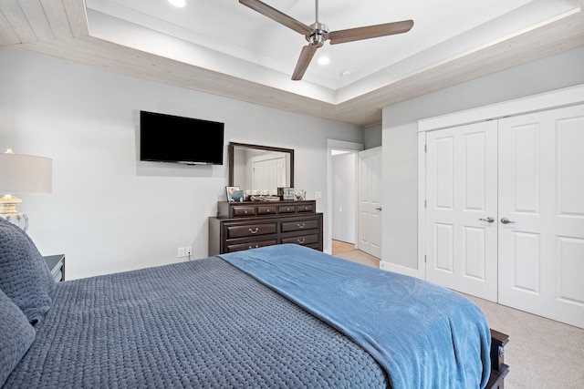 bedroom with ceiling fan, a raised ceiling, light carpet, and a closet