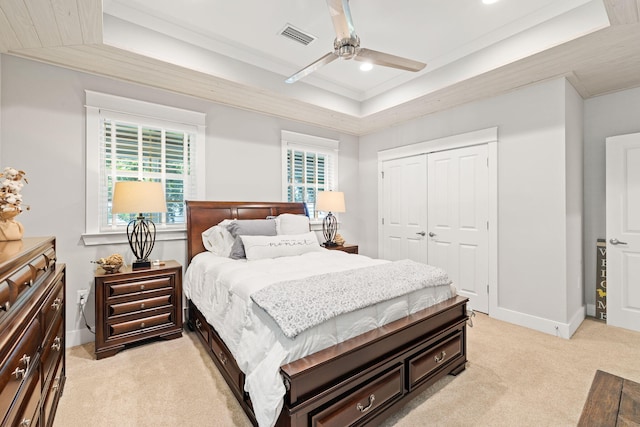 bedroom with a closet, light colored carpet, ceiling fan, and a tray ceiling