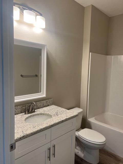 full bathroom with hardwood / wood-style flooring, shower / tub combination, vanity, and toilet