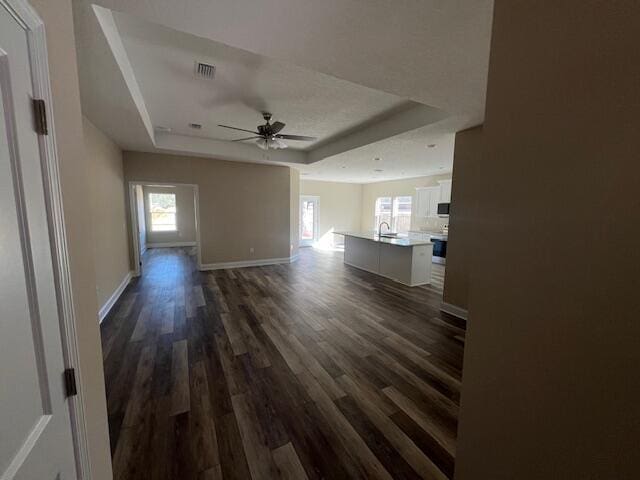 unfurnished living room with dark hardwood / wood-style floors, ceiling fan, and a tray ceiling