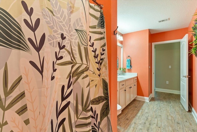 bathroom with a shower with curtain, wood-type flooring, a textured ceiling, toilet, and vanity