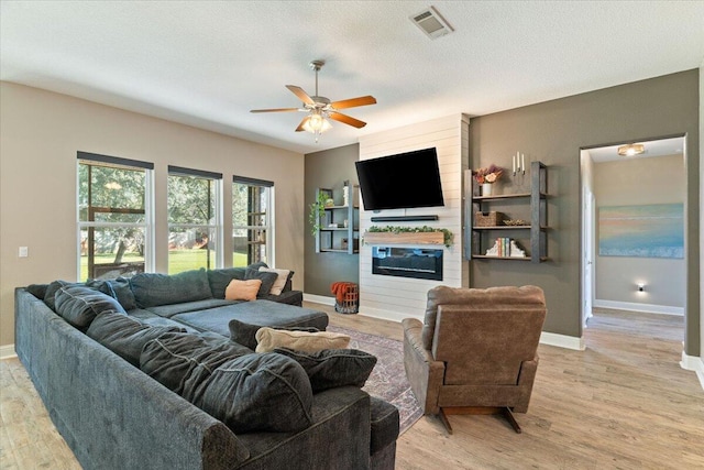 living room featuring a textured ceiling, a large fireplace, light hardwood / wood-style flooring, and ceiling fan