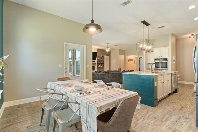 dining space with ceiling fan with notable chandelier, light hardwood / wood-style floors, and sink