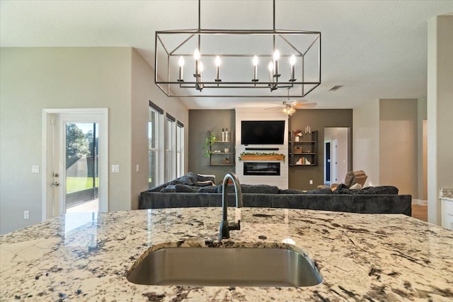 kitchen featuring sink, ceiling fan, light stone countertops, a textured ceiling, and decorative light fixtures