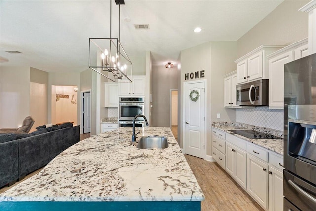 kitchen with appliances with stainless steel finishes, a kitchen island with sink, sink, light hardwood / wood-style flooring, and white cabinets