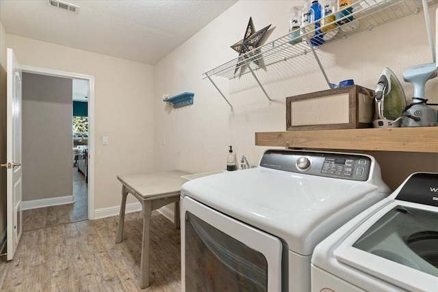 laundry area with a textured ceiling, light hardwood / wood-style floors, and washing machine and clothes dryer