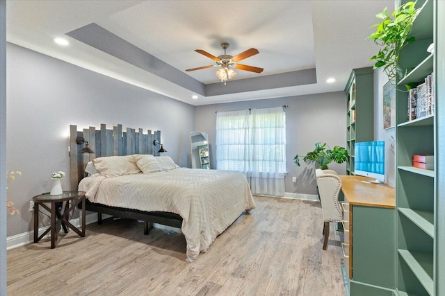 bedroom featuring ceiling fan, light hardwood / wood-style floors, and a tray ceiling