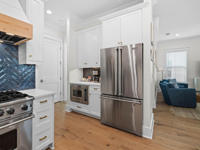 kitchen with backsplash, premium appliances, white cabinets, and premium range hood