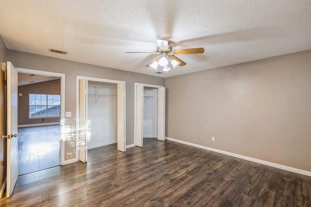 unfurnished bedroom featuring two closets, ceiling fan, dark hardwood / wood-style flooring, and a textured ceiling