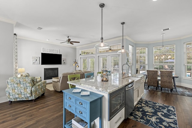 kitchen featuring pendant lighting, a wealth of natural light, an island with sink, stainless steel dishwasher, and light stone countertops