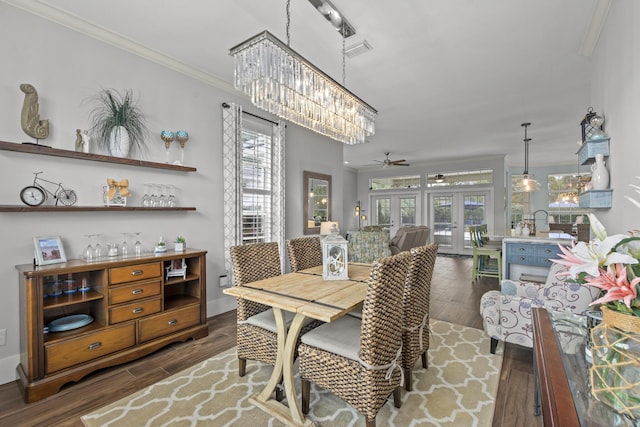 dining area featuring ceiling fan with notable chandelier, dark wood-type flooring, ornamental molding, and french doors