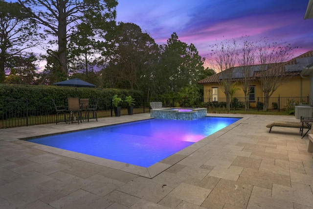 pool at dusk featuring an in ground hot tub and a patio area