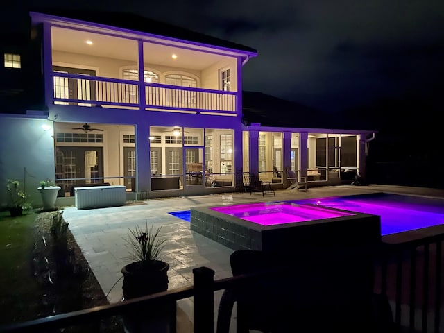 back house at twilight featuring a patio, a balcony, and an in ground hot tub