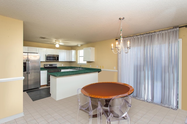 kitchen featuring stainless steel appliances, pendant lighting, a textured ceiling, white cabinets, and ceiling fan with notable chandelier